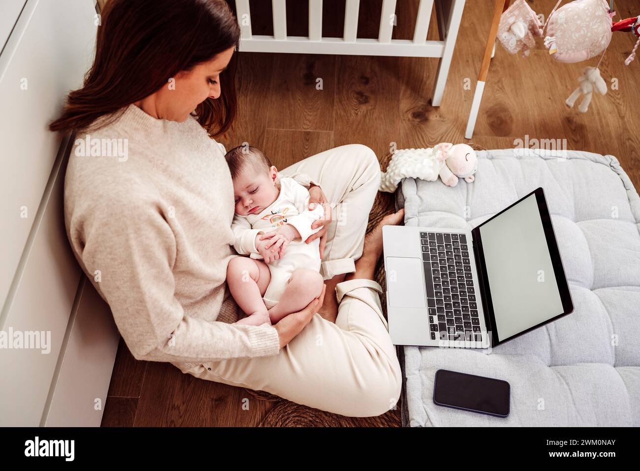 Mutter kümmert sich um das Baby und arbeitet mit dem Laptop im Home Office Stockfoto