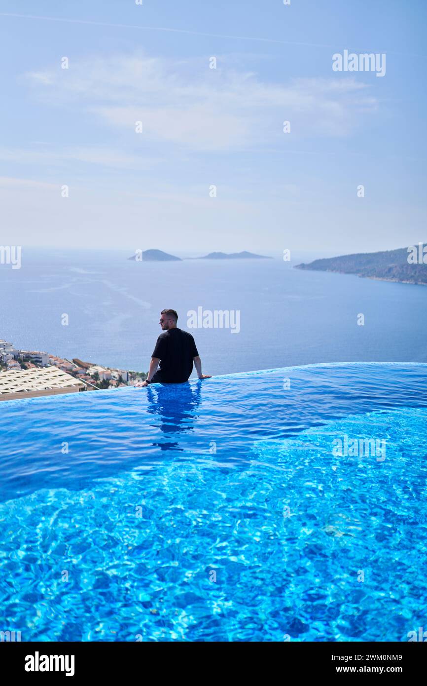Sorgloser Mann, der am Rand des blauen Swimmingpools in der Villa sitzt Stockfoto