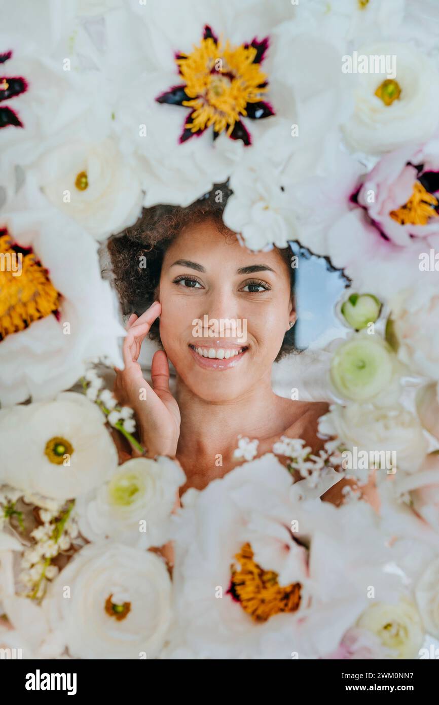 Lächelnde Frau, die unter Glasoberfläche mit Blumen liegt Stockfoto