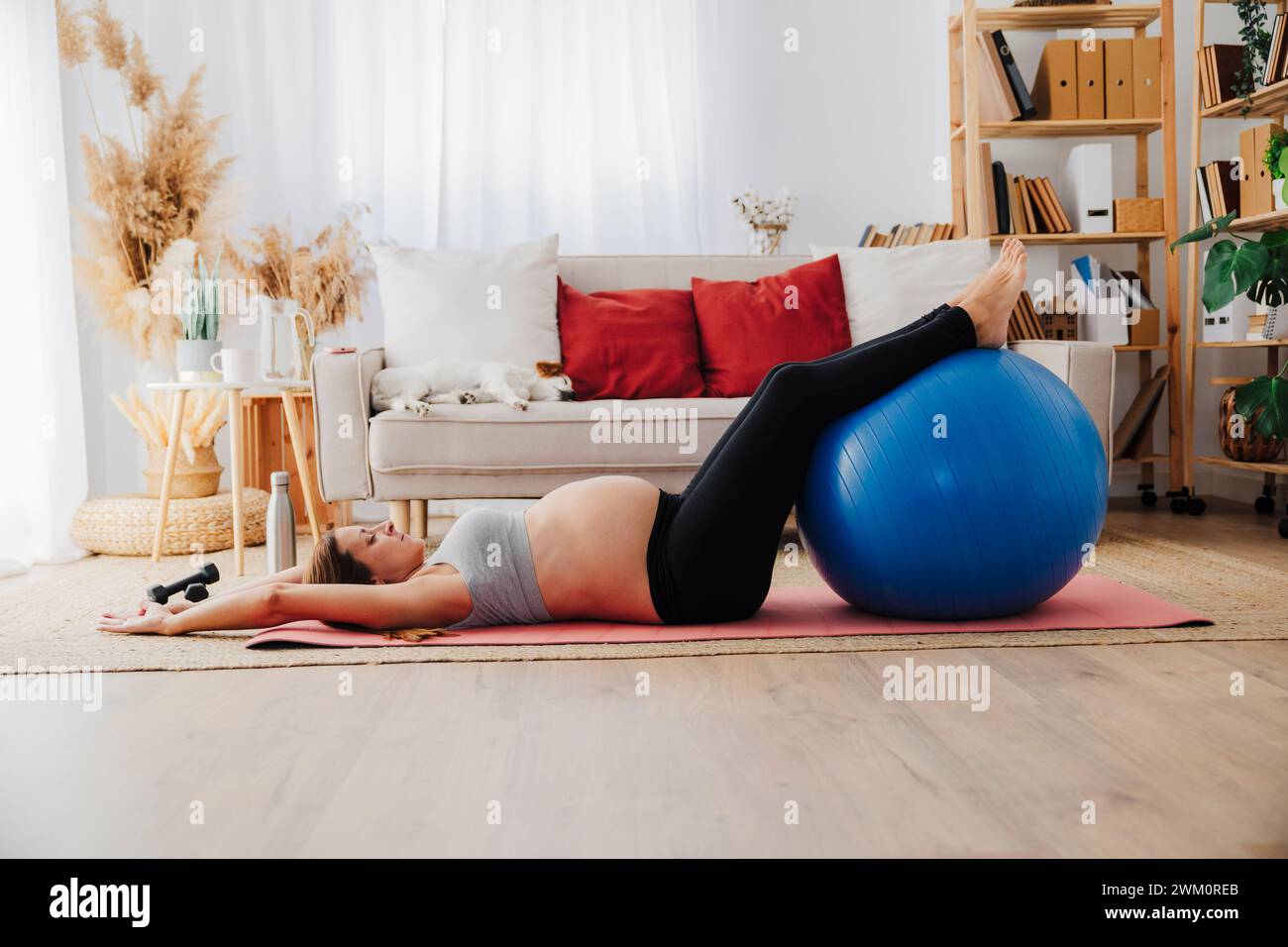 Schwangere Frau, die im Wohnzimmer mit Fitnessball auf einer Trainingsmatte liegt Stockfoto