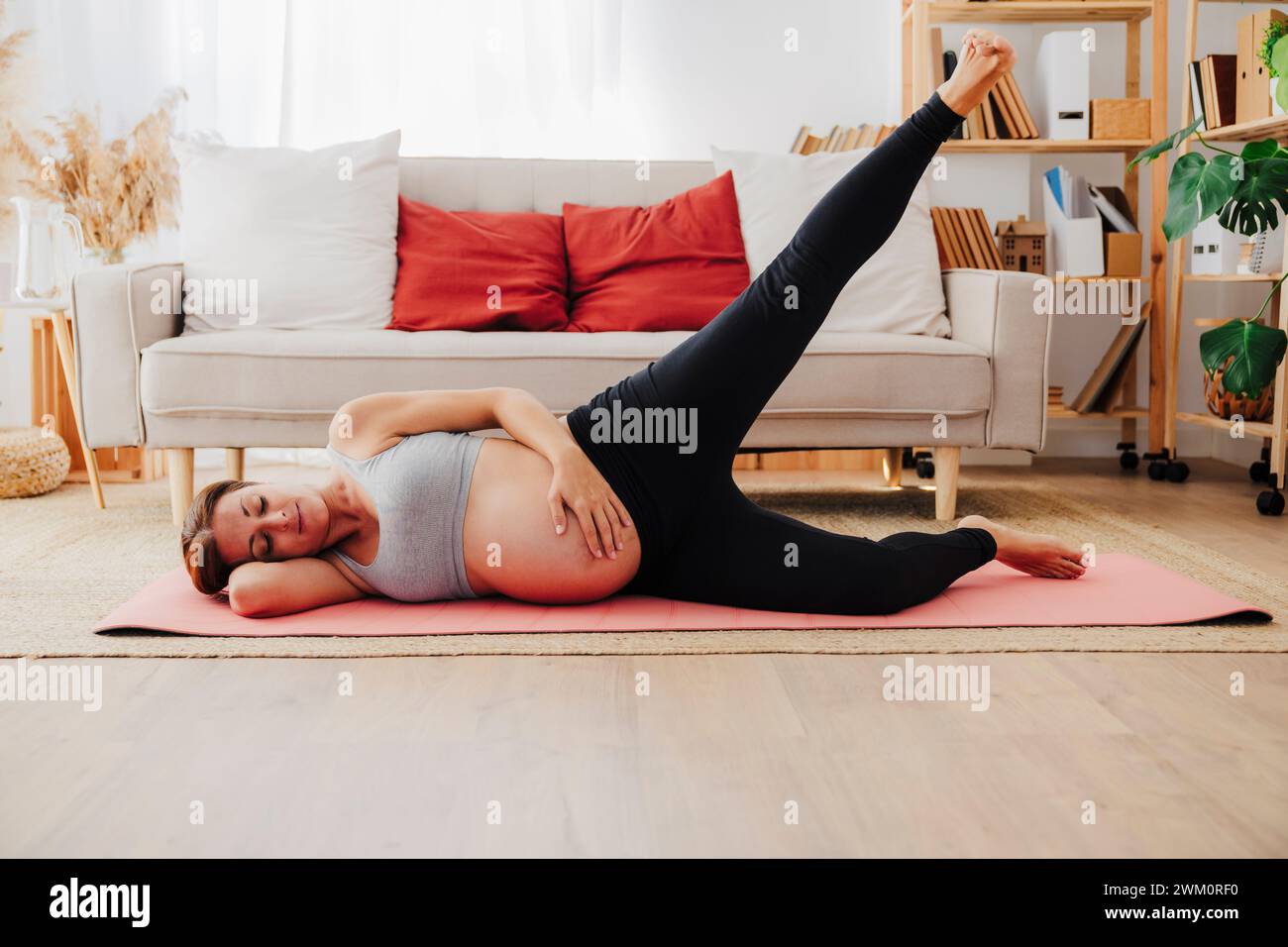Schwangere Frau, die auf Yogamatte liegt und zu Hause trainiert Stockfoto