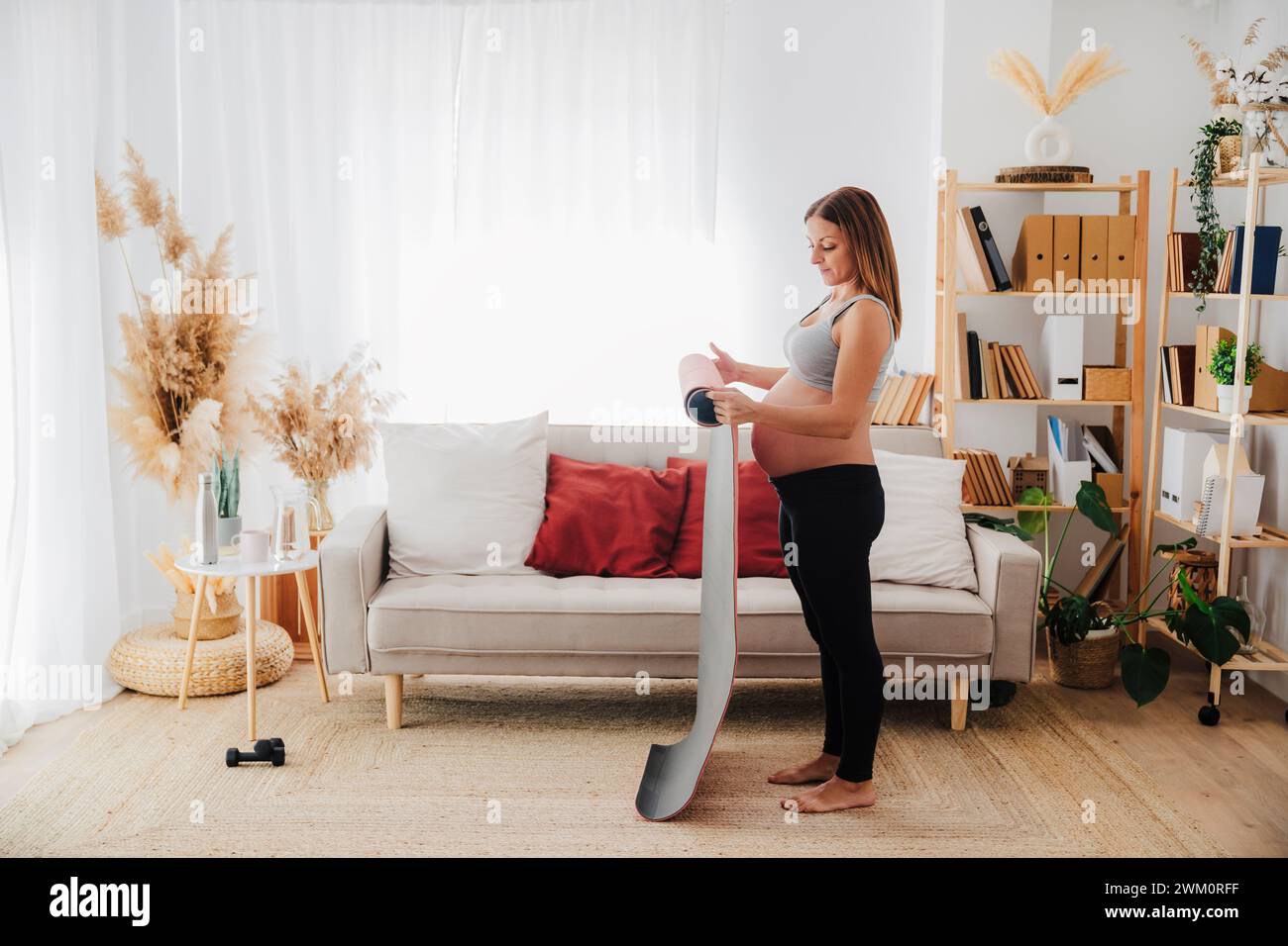Schwangere Frau rollende Yogamatte im Wohnzimmer zu Hause Stockfoto