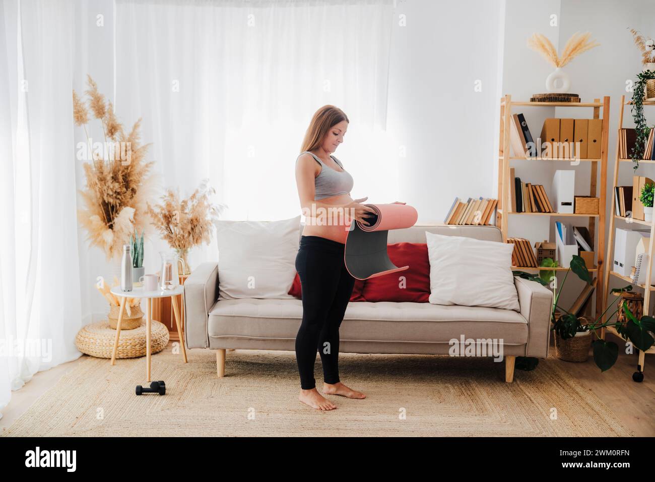 Schwangere Frau rollende Yogamatte im Wohnzimmer Stockfoto