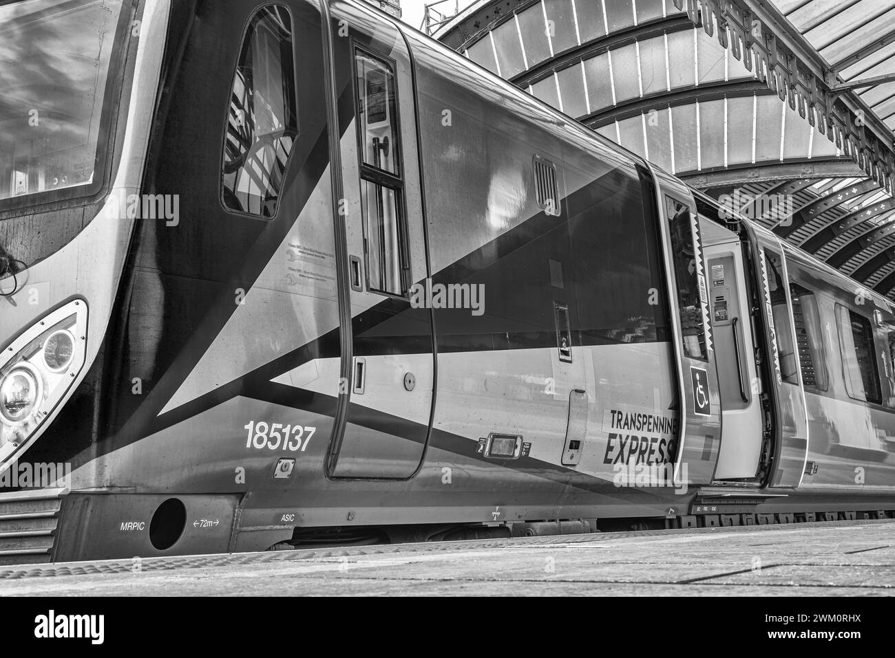 Flacher Blick auf einen Zug an einem Bahnsteig, der auf die Abfahrt wartet. Eine Wagentür ist offen und ein historischer Metallbogen ist darüber. Stockfoto