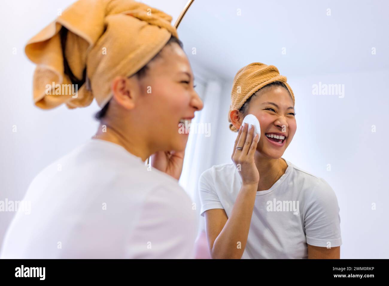 Fröhliche Frau reinigt das Gesicht mit einem Wattestäbchen vor dem Spiegel zu Hause Stockfoto