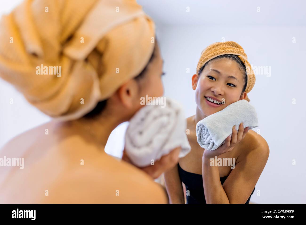 Lächelnde junge Frau, die das Gesicht mit einem Handtuch im Badezimmer zu Hause abwischt Stockfoto