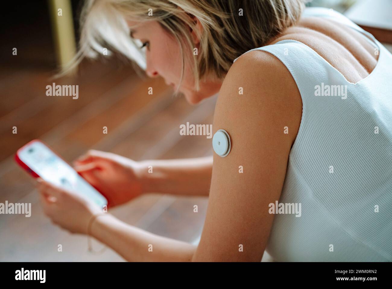 Blutzuckersensor am Arm der Frau mit Smartphone zu Hause Stockfoto