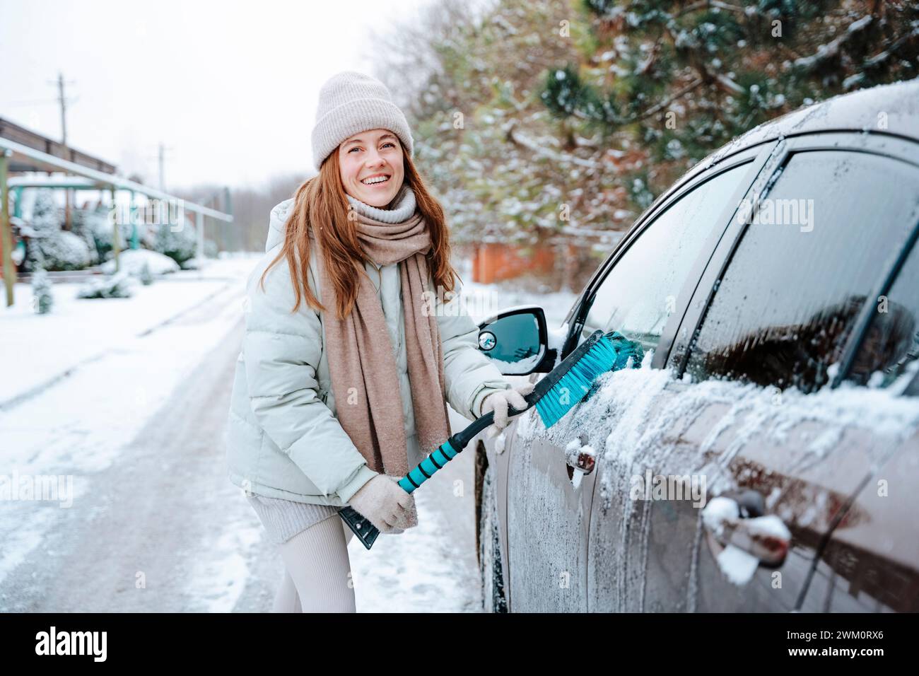 Lächelnde Frau, die im Winter Auto mit Besen putzt Stockfoto