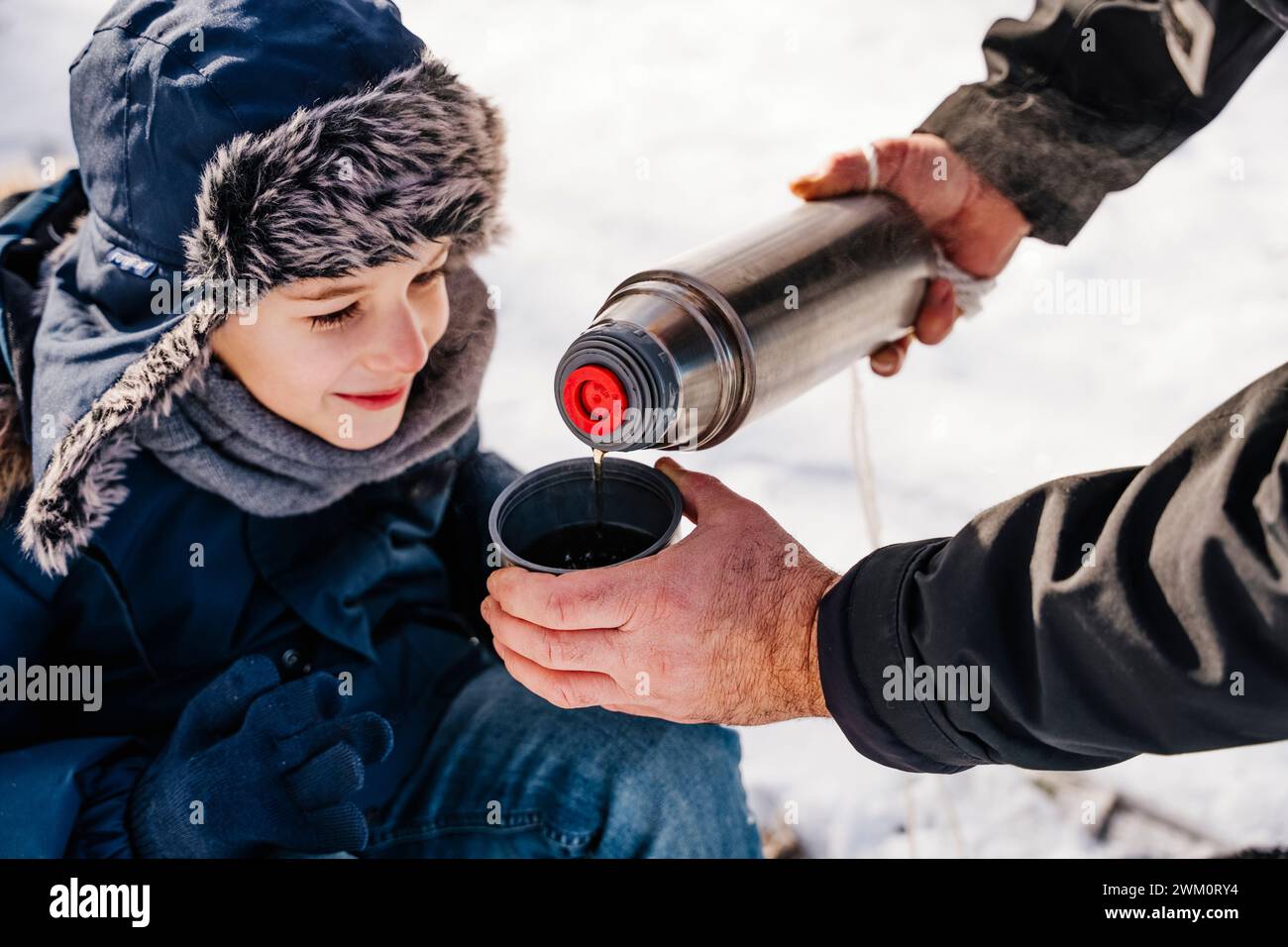 Vater gießt heißen Tee in eine Tasse für den Sohn im Winter Stockfoto