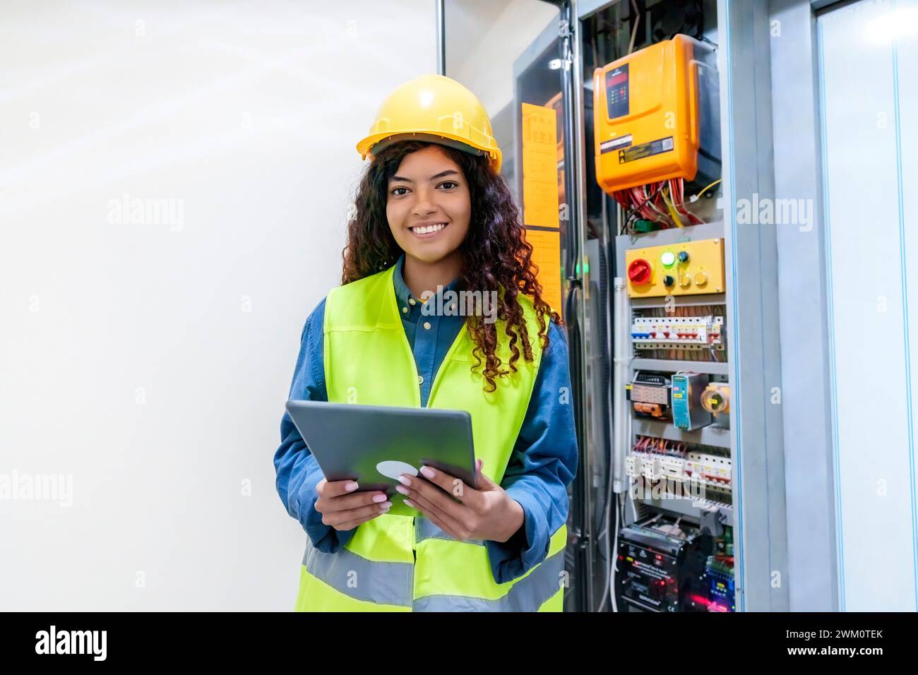 Ein lächelnder Ingenieur hält den Tablet-PC am elektrischen Sicherungskasten Stockfoto