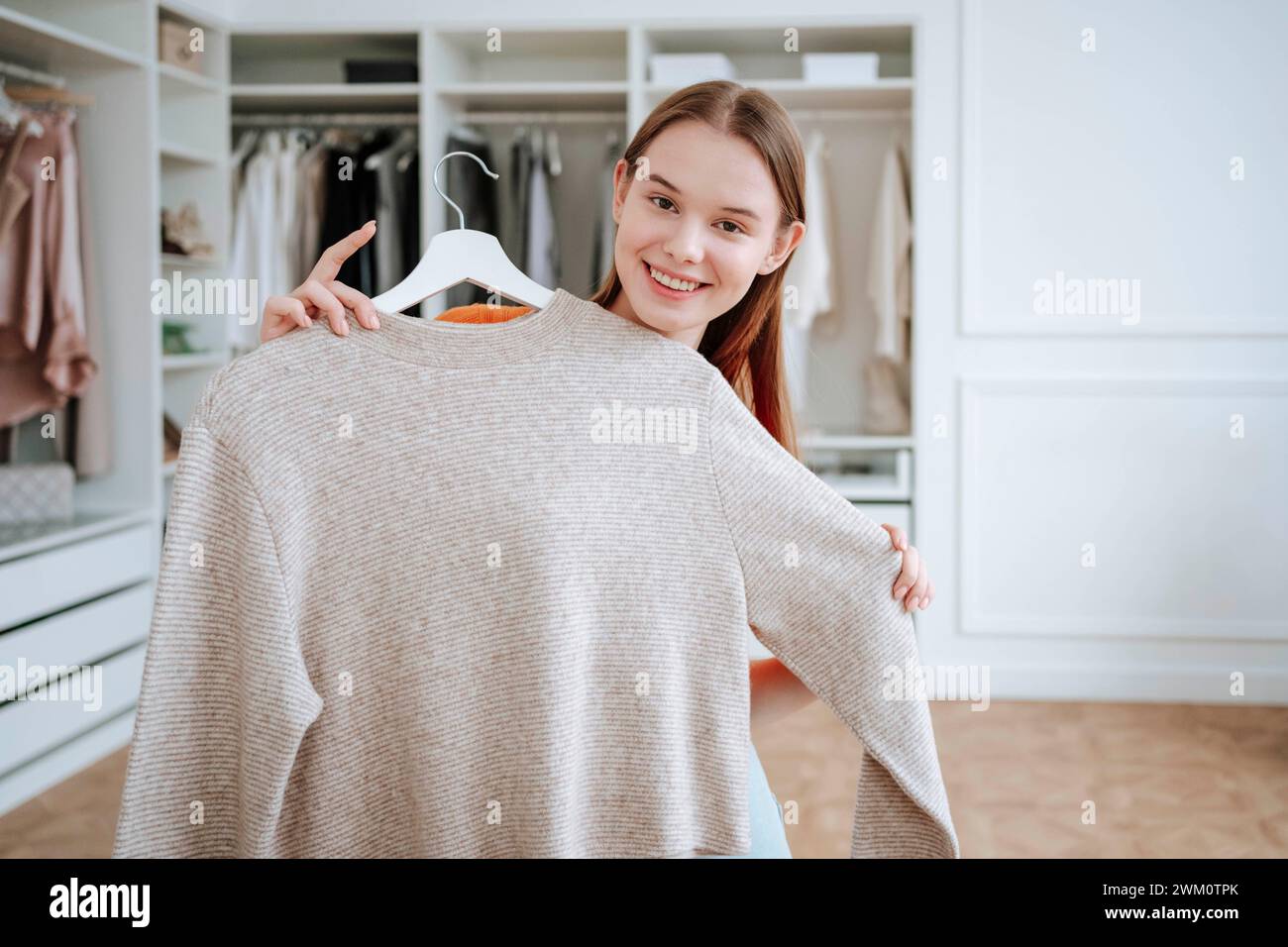Lächelnde Frau, die ein T-Shirt in der Nähe des Kleiderschranks hält Stockfoto