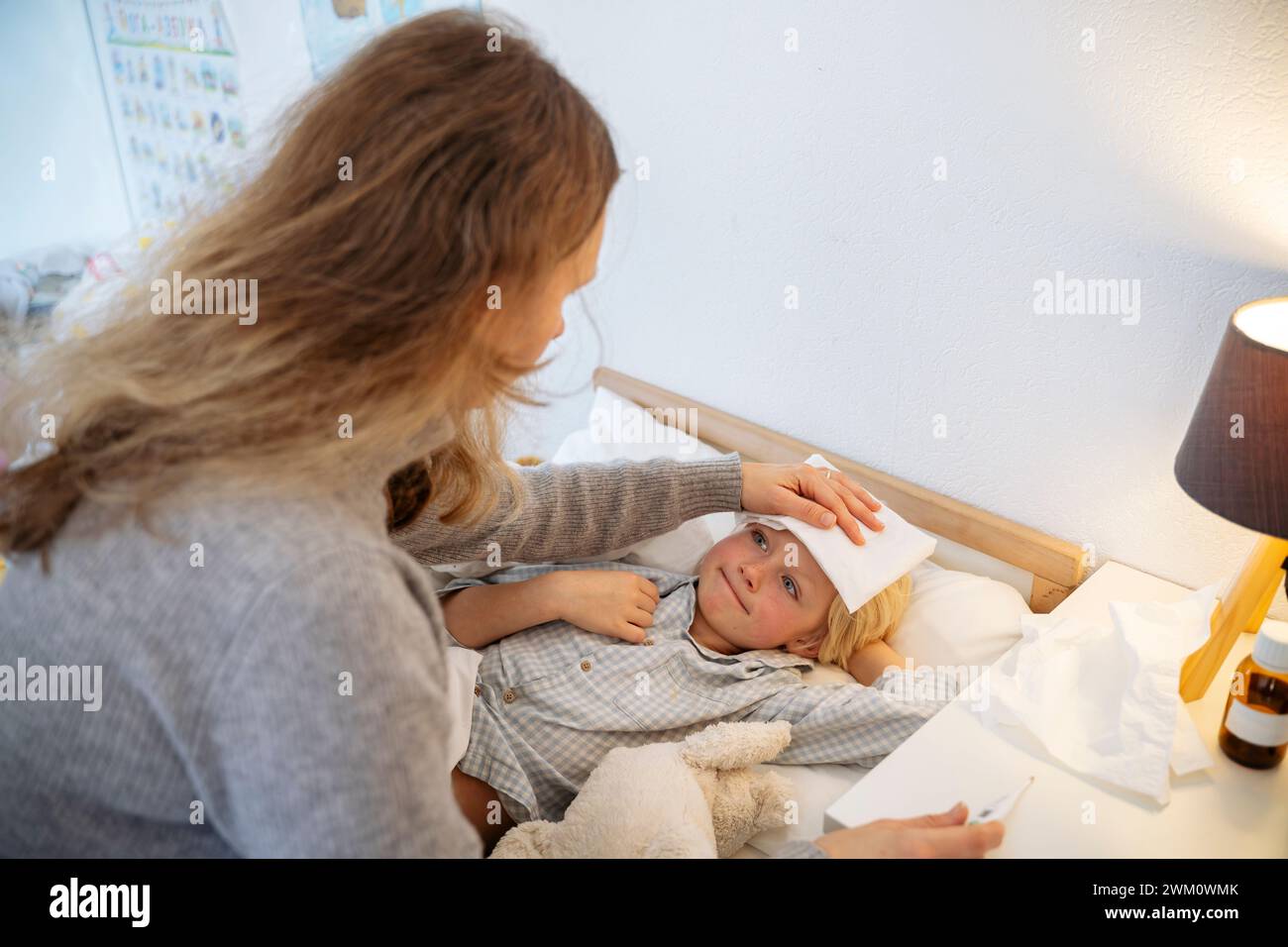 Mutter, die Kompresse auf die Stirn des Sohnes legt, liegt zu Hause auf dem Bett Stockfoto