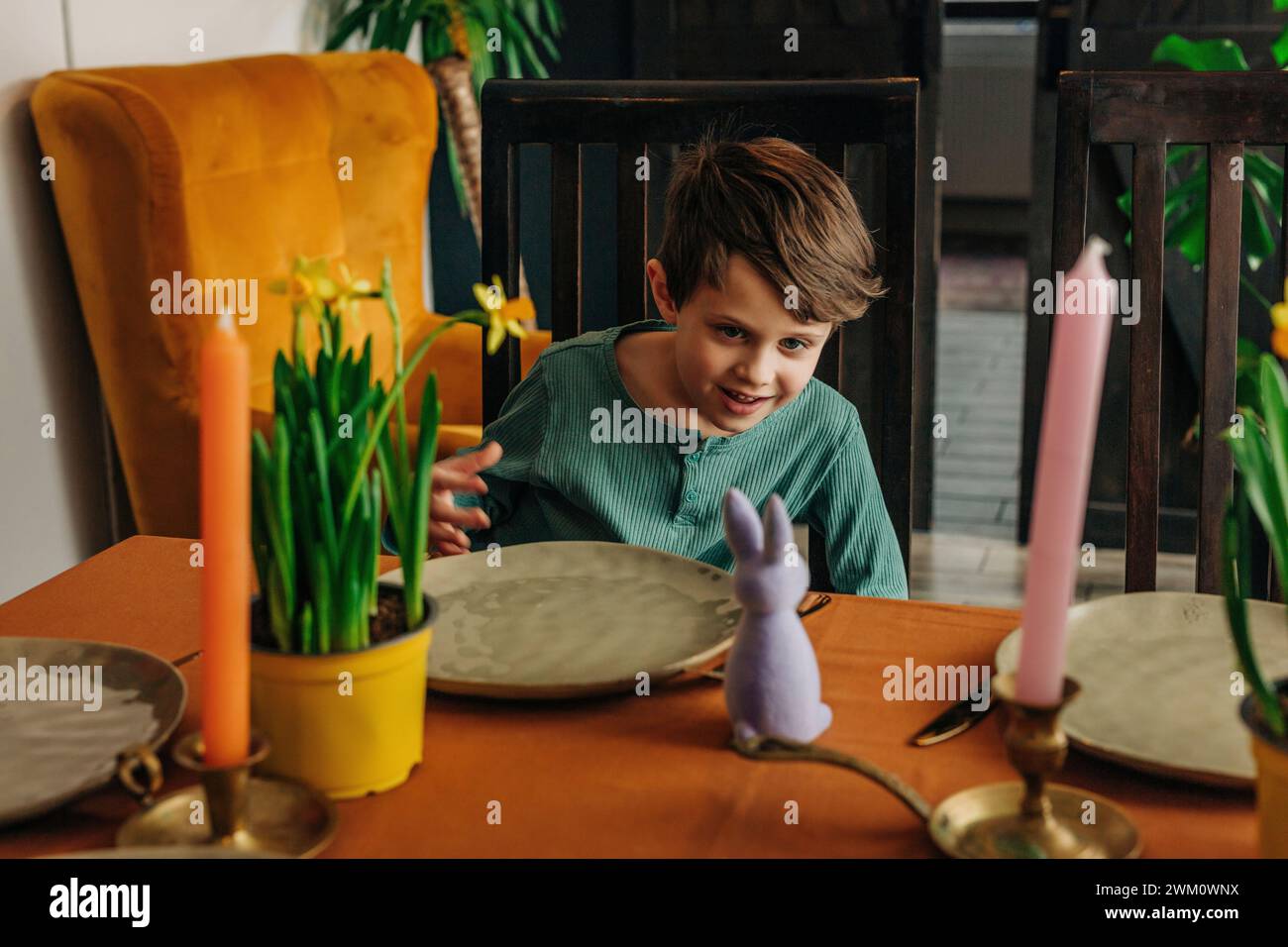 Ein lächelnder Junge, der Osterhasen am Esstisch zuhause ansieht Stockfoto