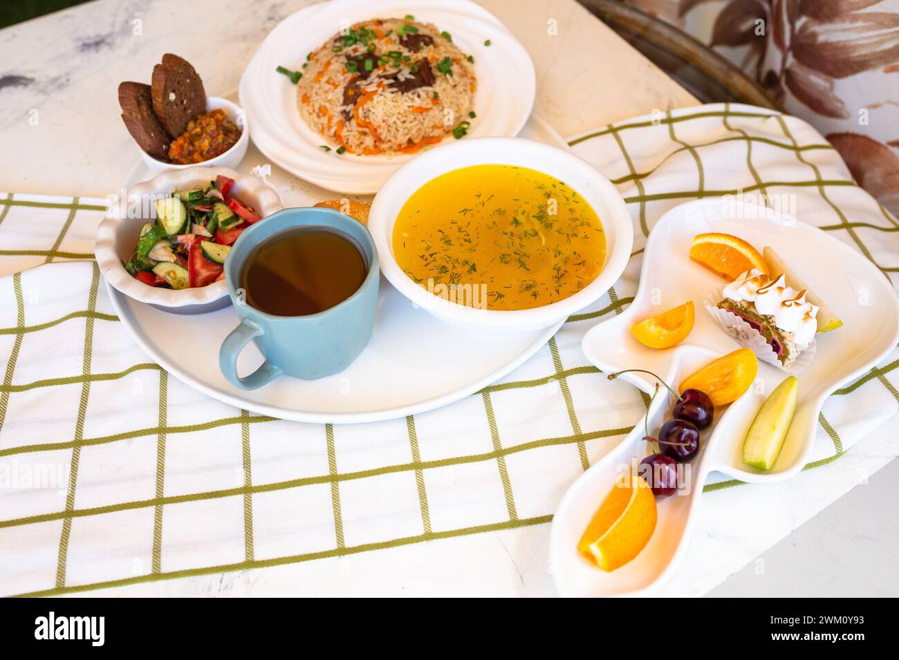 Usbekische Nationalgerichte, Plov, Shurpa, Salat und nicht auf einem Tablett mit Tee. Traditionelle usbekische Küche. Hintergrund mit kariertem Tischtuch. Stockfoto