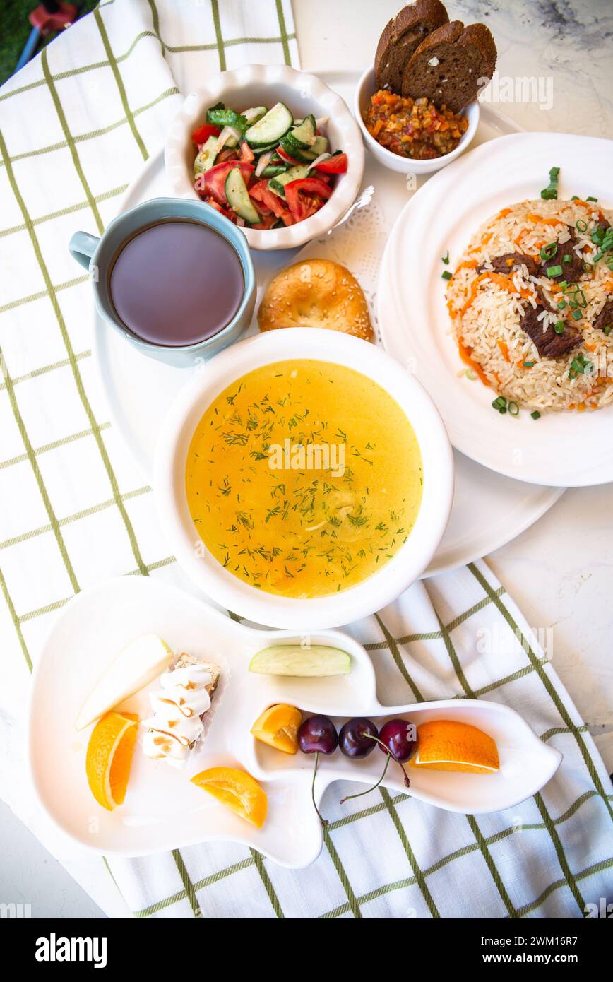 Usbekische Nationalgerichte, Plov, Shurpa, Salat und nicht auf einem Tablett mit Tee. Traditionelle usbekische Küche. Hintergrund mit kariertem Tischtuch. Stockfoto