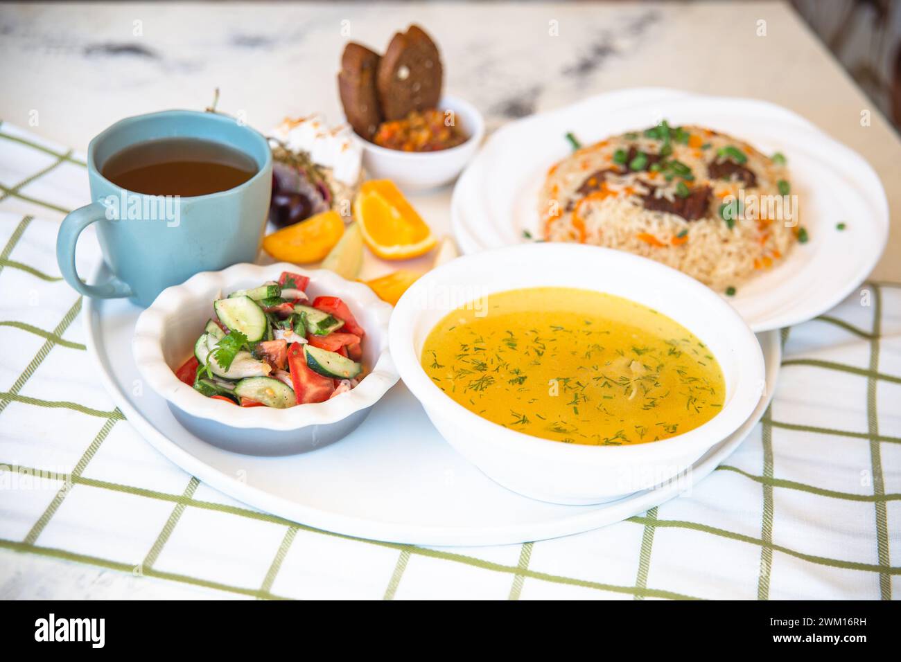Usbekische Nationalgerichte, Plov, Shurpa, Salat und nicht auf einem Tablett mit Tee. Traditionelle usbekische Küche. Hintergrund mit kariertem Tischtuch. Stockfoto