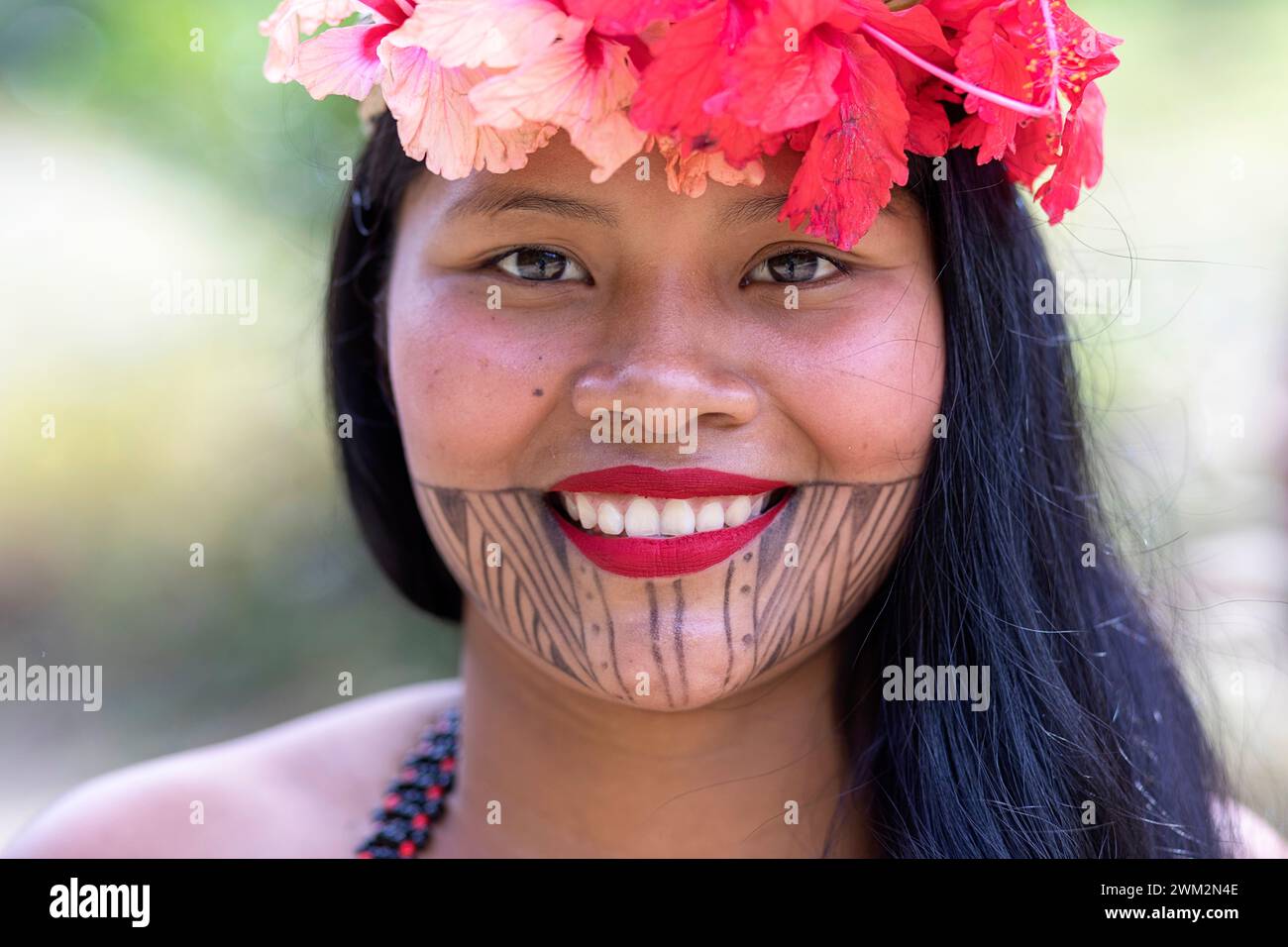 Lächelnde junge Frau aus dem Stamm der Embera aus einem Dorf im Chagres-Nationalpark mit traditionellen Tattoos im Gesicht und Blumen im Haar, Panama Stockfoto