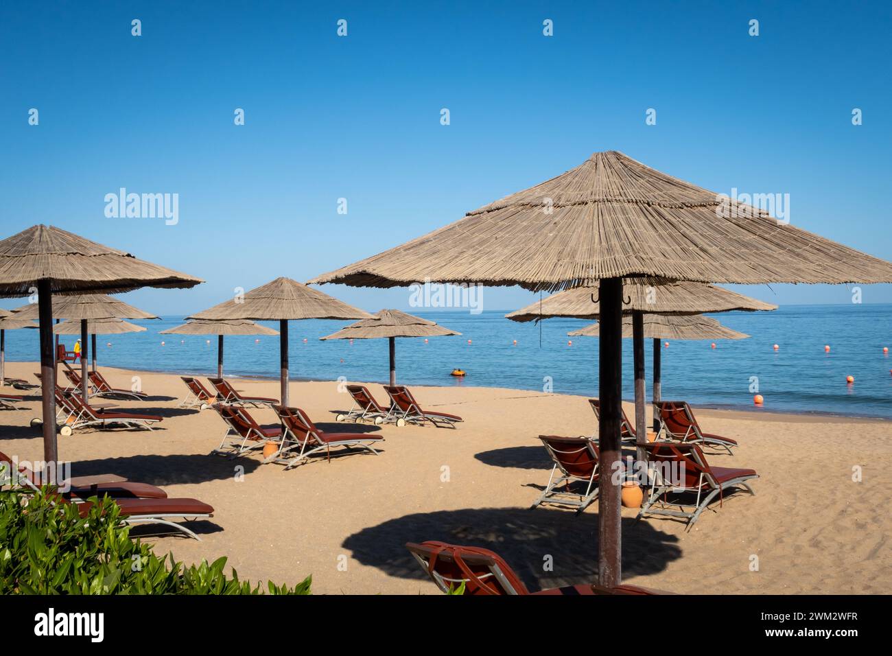 Sandstrand in Fujairah, Vereinigte Arabische Emirate, mit Strohschirmen und Sonnenliegen, Meerblick und blauem Himmel, keine Leute. Stockfoto