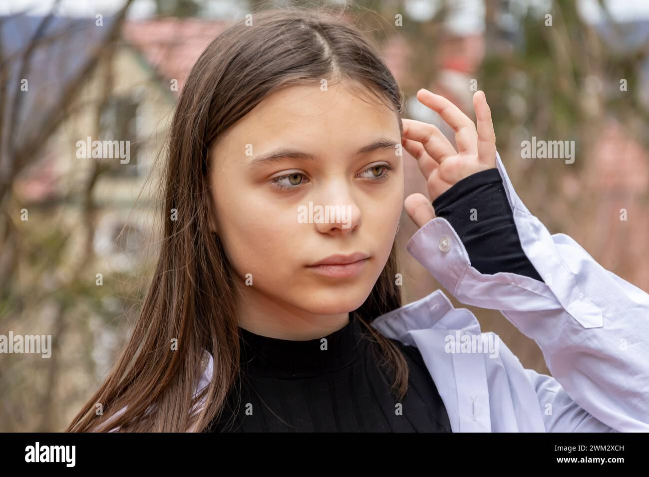 Ein Porträt eines schönen Teenagers von 11-13 Jahren, das ihre Haare mit der Hand auf dem Hintergrund einer Landlandschaft fixiert. Stockfoto