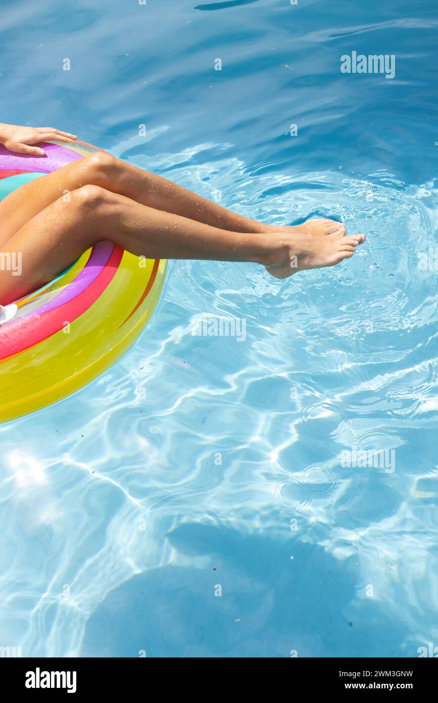 Person genießt ein entspannendes Bad in einem Pool an einem sonnigen Tag, die Beine ruhen auf einem farbenfrohen Schwimmer Stockfoto