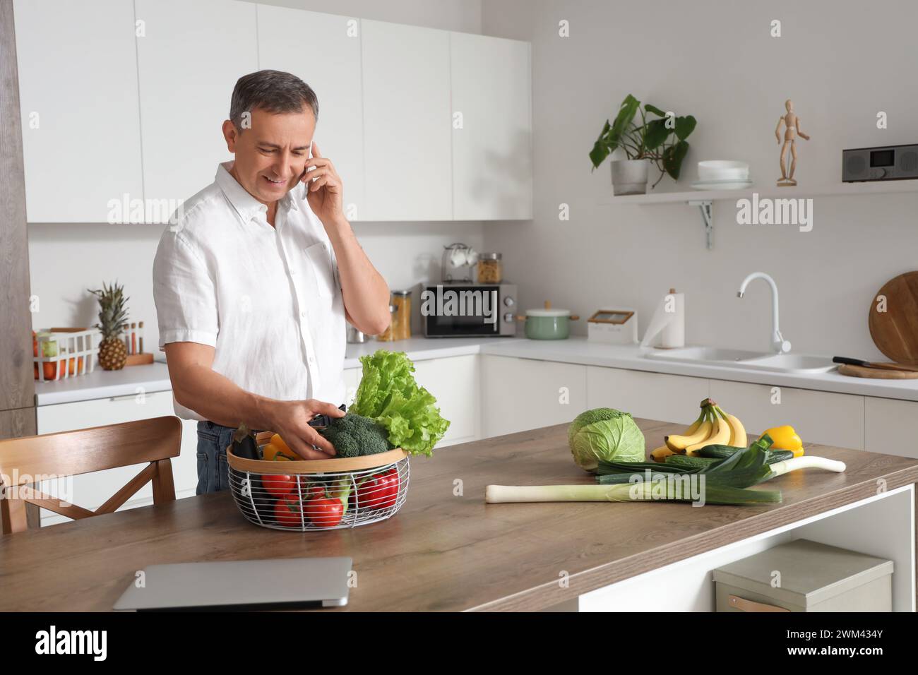 Reifer Mann mit frischem Gemüse, der mit dem Handy in der Küche spricht Stockfoto