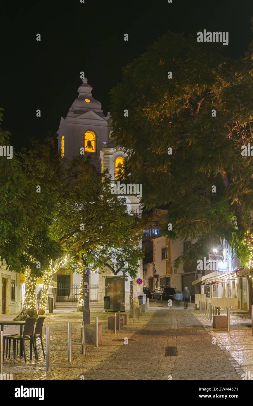 Nächtliche Stadtlandschaft mit Bäumen vor dem Turm der katholischen Kirche Igreja de Santo Antonio in Lagos, Algarve, Portugal Stockfoto