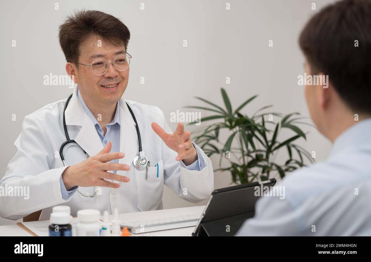 Ein asiatischer Arzt mittleren Alters und ein männlicher Patient, der sich einer Krankenhausberatung unterzieht Stockfoto