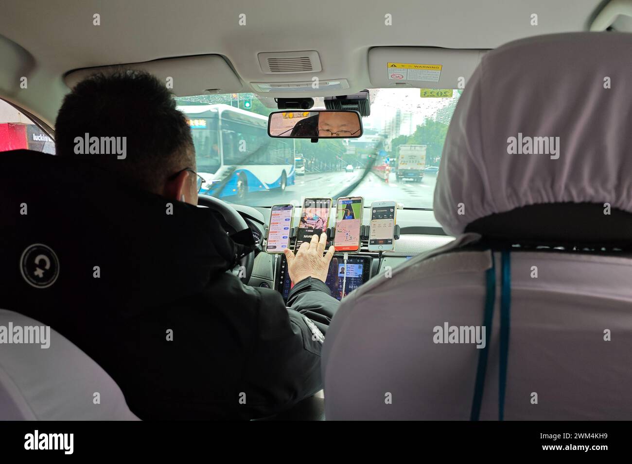 SHANGHAI, CHINA - 24. FEBRUAR 2024 - ein online fahrender Fahrer hat fünf Mobiltelefone auf beiden Seiten des Fahrersitzes, um es einfacher zu nehmen Stockfoto