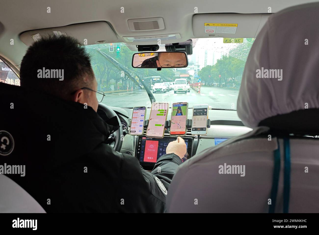 SHANGHAI, CHINA - 24. FEBRUAR 2024 - ein online fahrender Fahrer hat fünf Mobiltelefone auf beiden Seiten des Fahrersitzes, um es einfacher zu nehmen Stockfoto