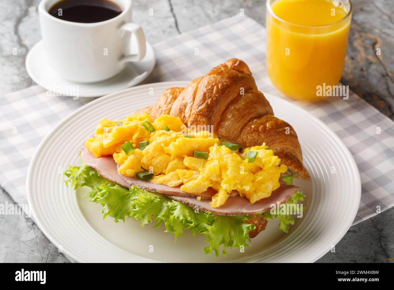 Gesundes Frühstückscroissant mit Rührei und Schinken serviert mit Orangensaft und Kaffee auf einem Marmortisch. Horizontal Stockfoto