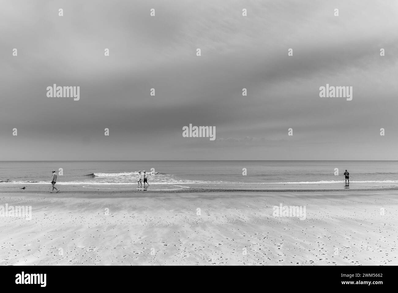 Gruppe von Menschen, die am Ufer entlang an einem Strand mit völlig bewölktem Himmel laufen Stockfoto
