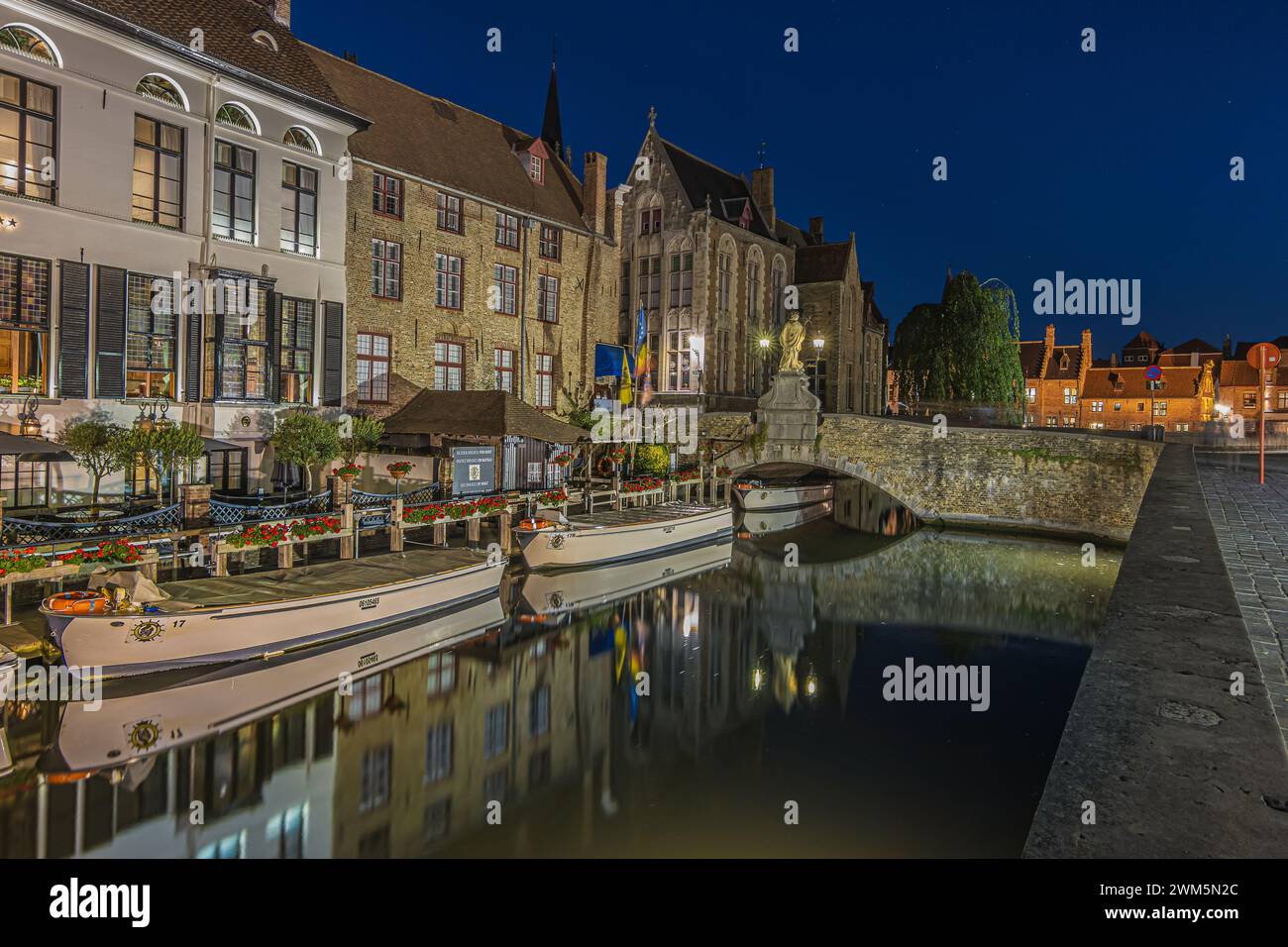 Beleuchtete Häuser am Kanal in Brügge am Abend. Hansestadt in Belgien zur blauen Stunde. Historische Kaufmannshäuser in der Hansestadt. Stockfoto