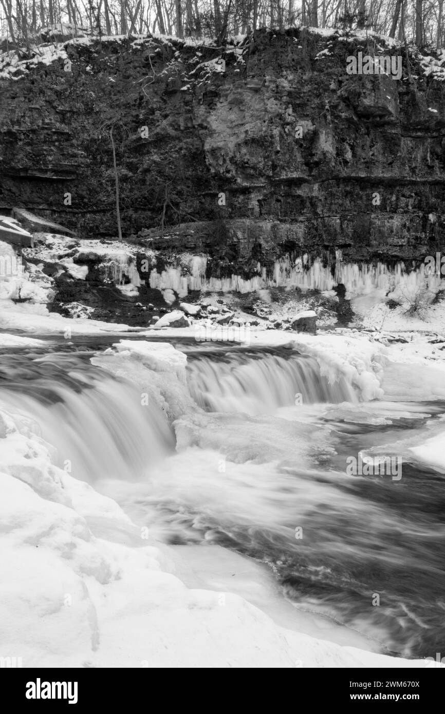 Lange Exposition teilweise gefrorener Wasserfall neben felsigen Klippen Stockfoto