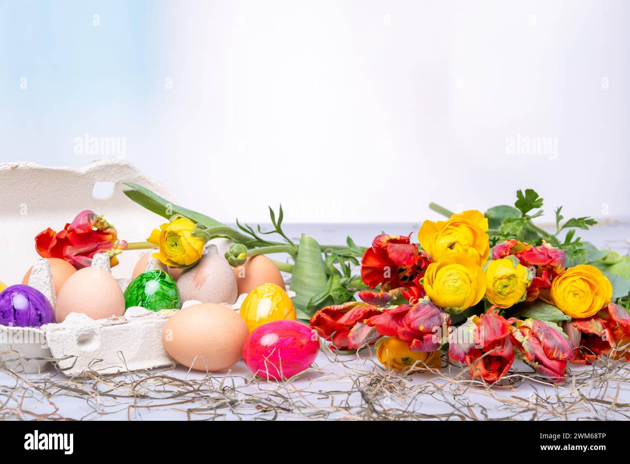 Bunte Ostereier auf einem Tisch mit Bumenstrauß als Postkartenmotiv zu Ostern Stockfoto