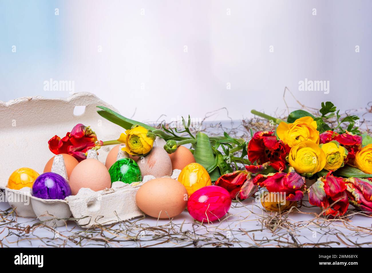 Bunte Ostereier auf einem Tisch mit Bumenstrauß als Postkartenmotiv zu Ostern Stockfoto