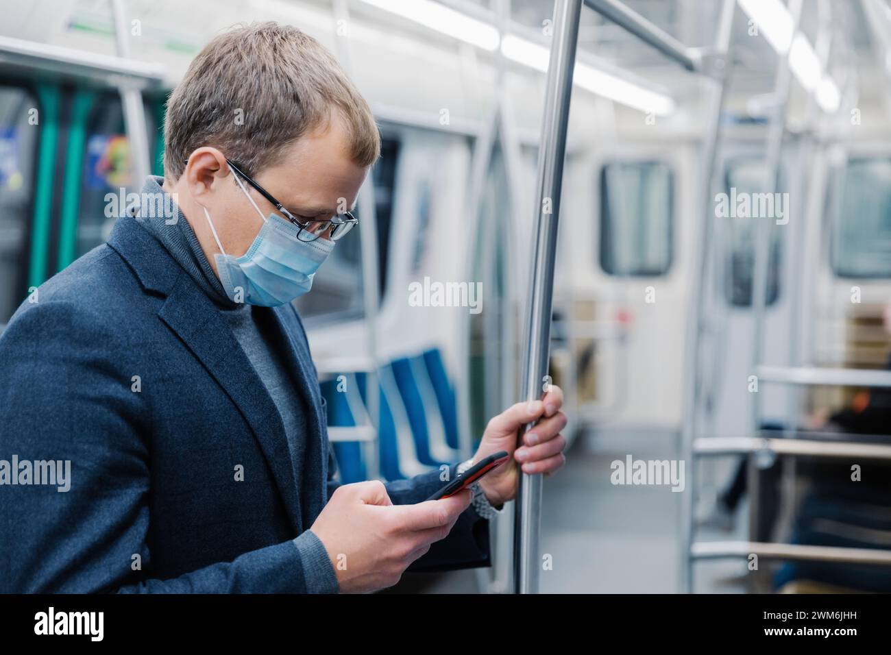 Maskierter Pendler in der U-Bahn mit Smartphone, vom Bildschirm absorbiert. Stockfoto