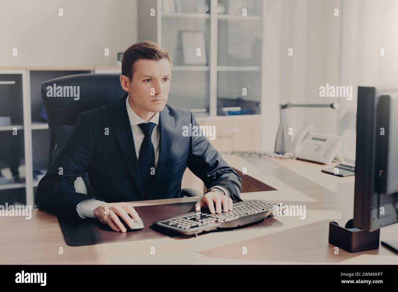 Ein konzentrierter Geschäftsmann an seinem Schreibtisch mit Computerbildschirmen, der Hingabe verkörpert. Stockfoto