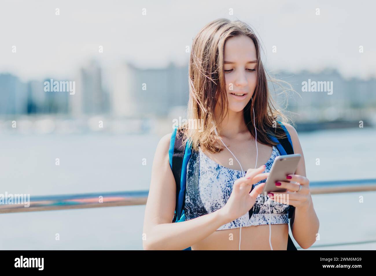 Durchdachte Joggerin in Sportbekleidung, die ihr Smartphone auf einer urbanen Uferterrasse benutzt. Stockfoto