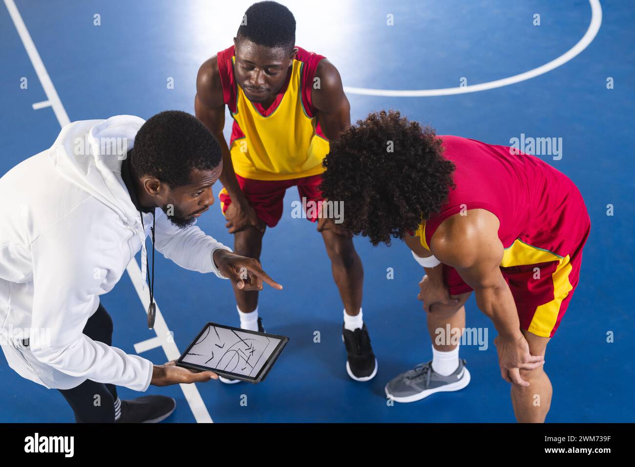 Der afroamerikanische Coach diskutiert mit Basketballspielern auf dem Spielfeld über Strategie Stockfoto