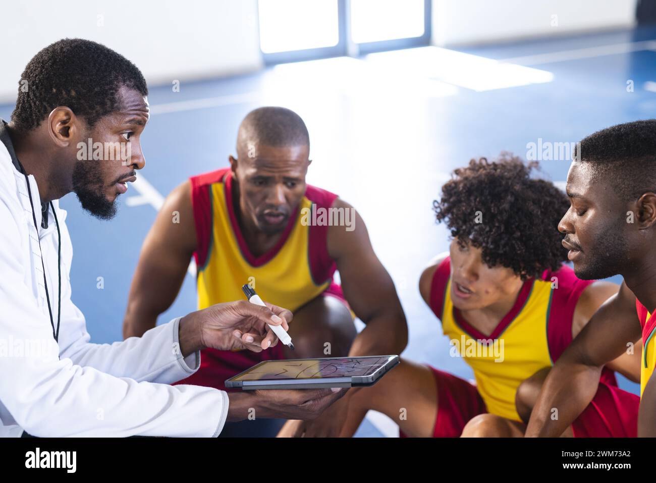 Afroamerikanischer Trainer diskutiert Strategie mit Basketballspielern auf dem Platz Stockfoto