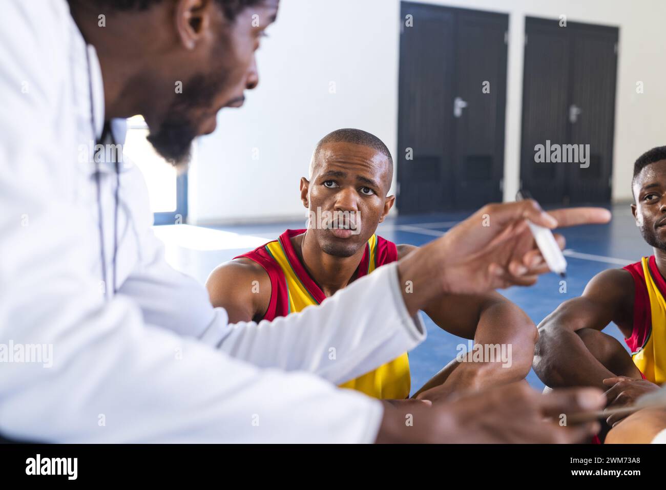 Afroamerikanischer Trainer diskutiert Strategie mit Spielern in einem Fitnessstudio Stockfoto