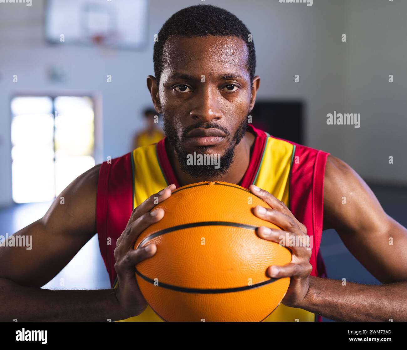 Fokussierter afroamerikanischer Mann, der einen Basketball in einem Fitnessstudio hält Stockfoto