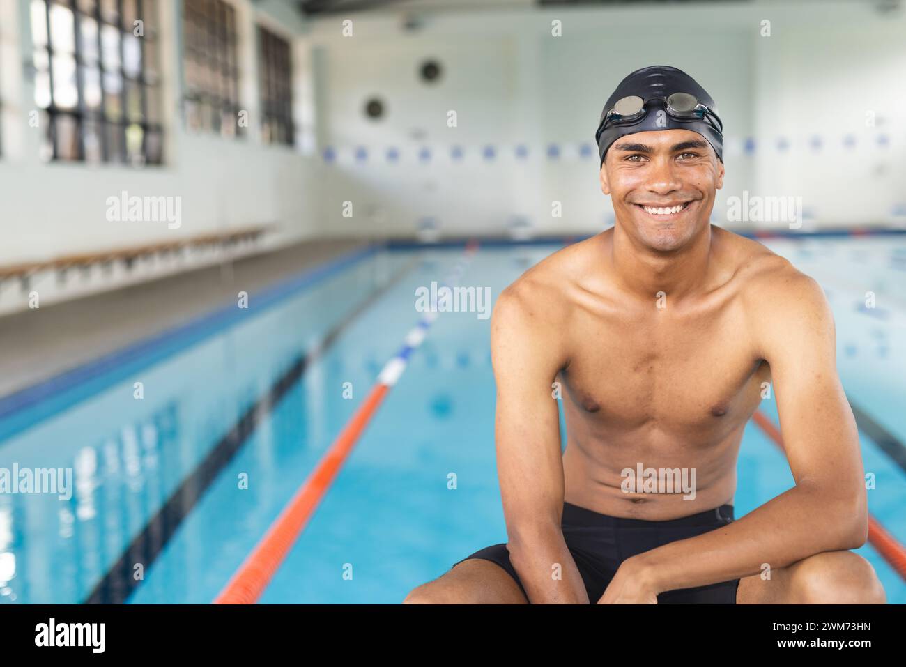 Junger männlicher Sportler, der mit birassischem Geschlecht schwimmt, lächelt am Pool, mit Kopierraum Stockfoto