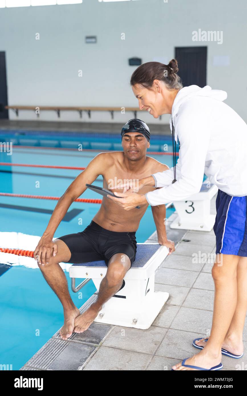 Die Trainerin einer weißen Frau gibt einem jungen, birassischen Mann am Pool Feedback Stockfoto