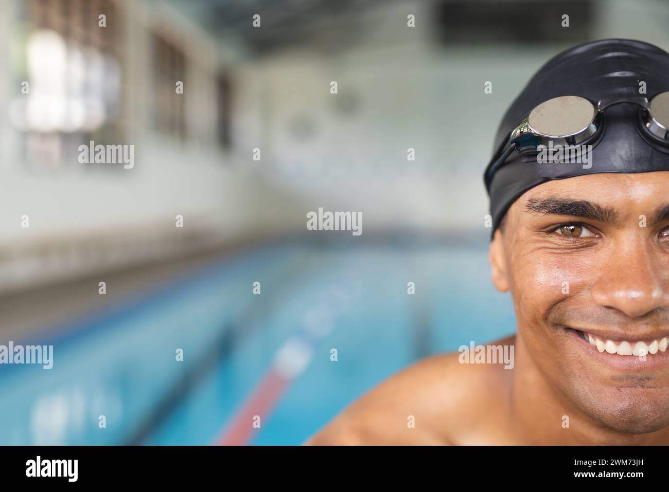 Junger männlicher Sportler, der mit birassischem Geschlecht schwimmt, lächelt am Pool und hat Platz für Kopien Stockfoto