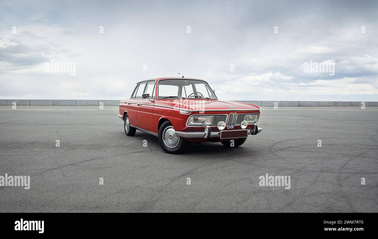 Roter Klassiker BMW aus den 1960er Jahren Dreiviertelansicht der deutschen Limousine vor bewölktem Himmel. Stockfoto