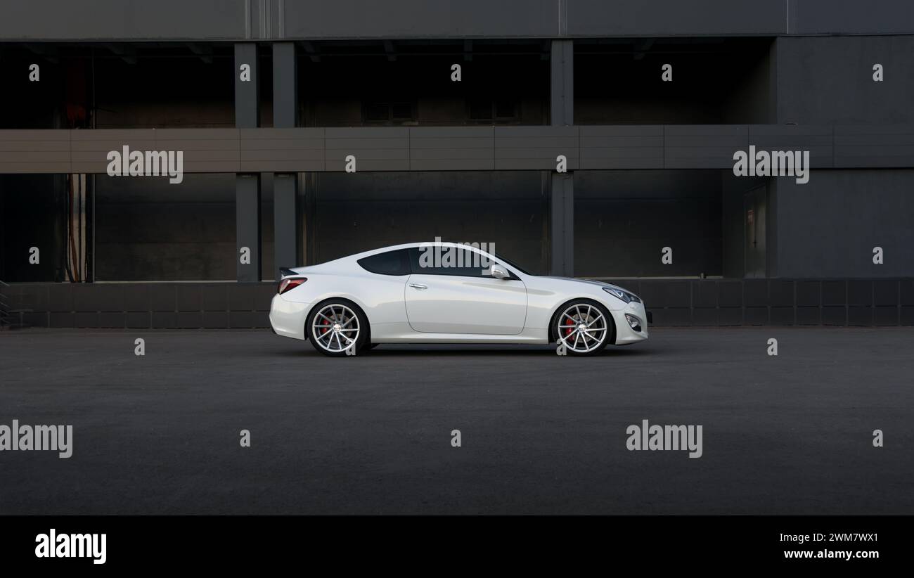 Weißes Hyundai Genesis Coupe vor der dunkelgrauen Wand. Seitenprofil des sportlichen koreanischen Coupés in urbaner Umgebung. Stockfoto
