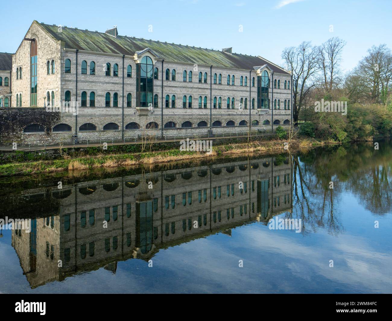 Büros mit ebenerdigen Parkplätzen im traditionellen Stil, die sich an einem hellen, sonnigen Wintertag mit Bäumen im Fluss Kent spiegeln Stockfoto