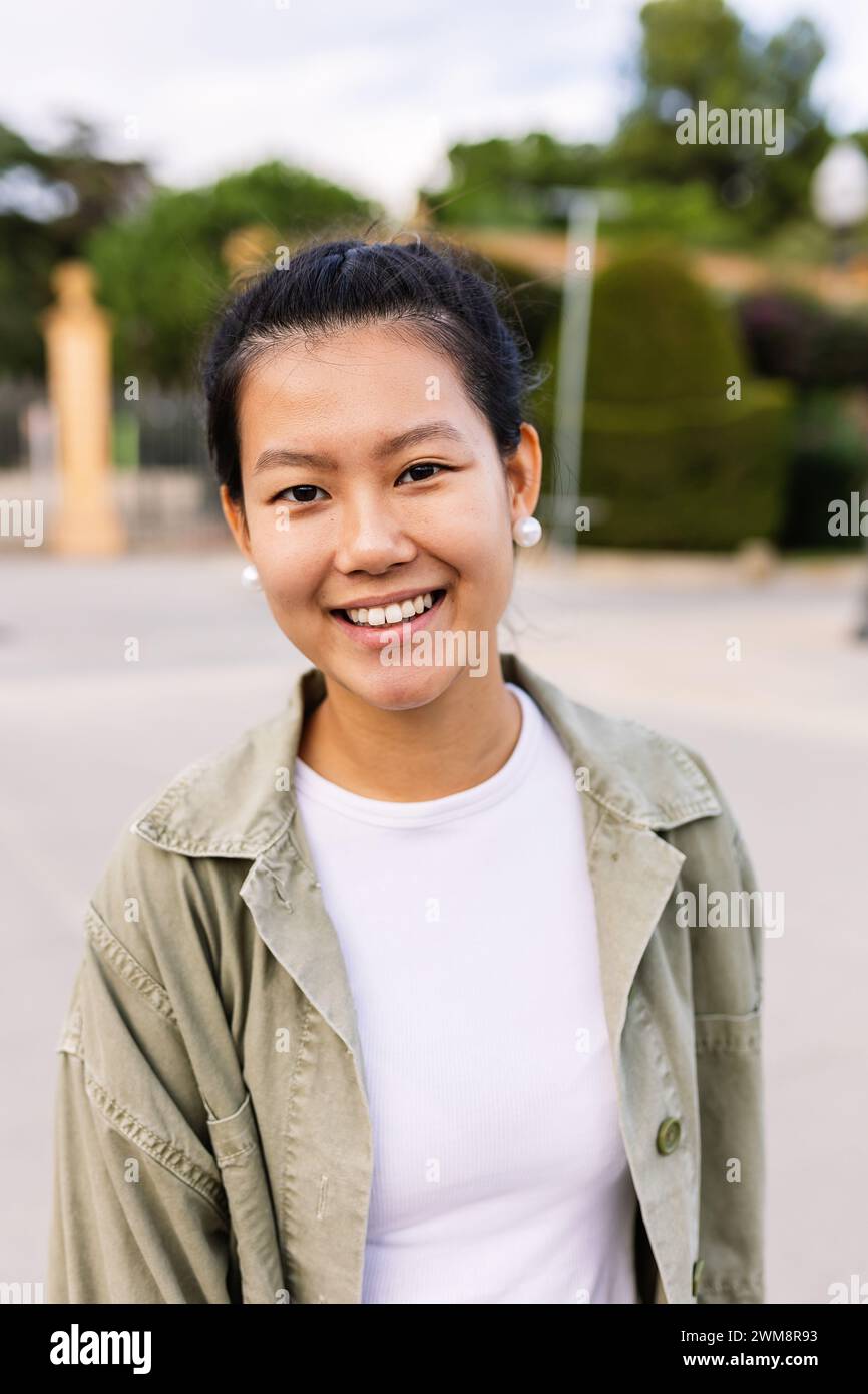 Glückliches junges asiatisches Mädchen lächelt in die Kamera, steht auf der Stadtstraße Stockfoto