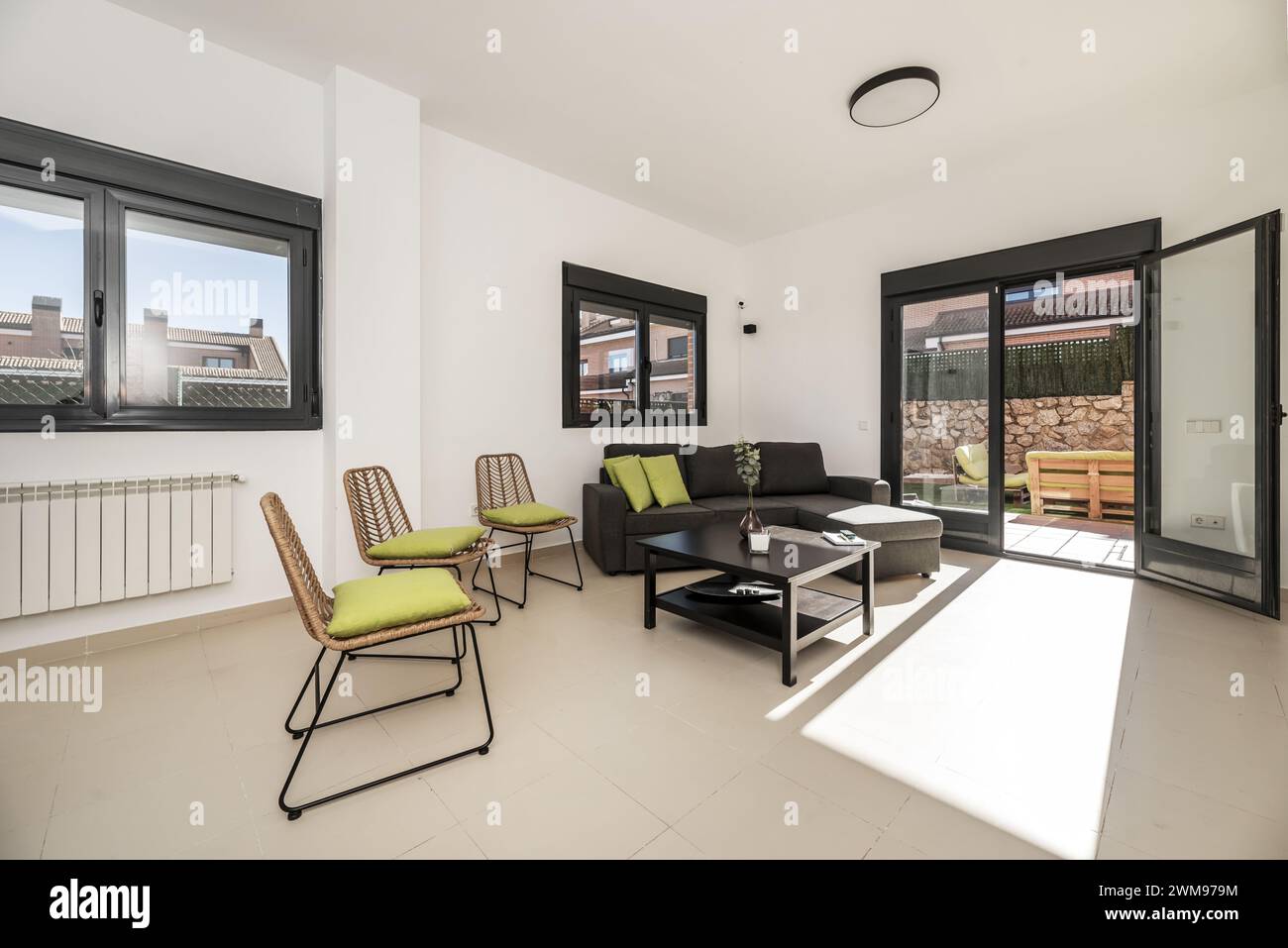 Wohnzimmer eines Einfamilienhauses mit glatten, weiß lackierten Wänden, einem Sitzbereich mit einer Chaiselonge mit grauem Stoff und schwarzem Aluminium Stockfoto